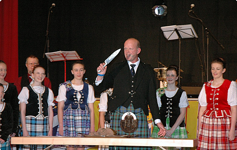 Man ready to cut the haggis, surrounded by dancers.